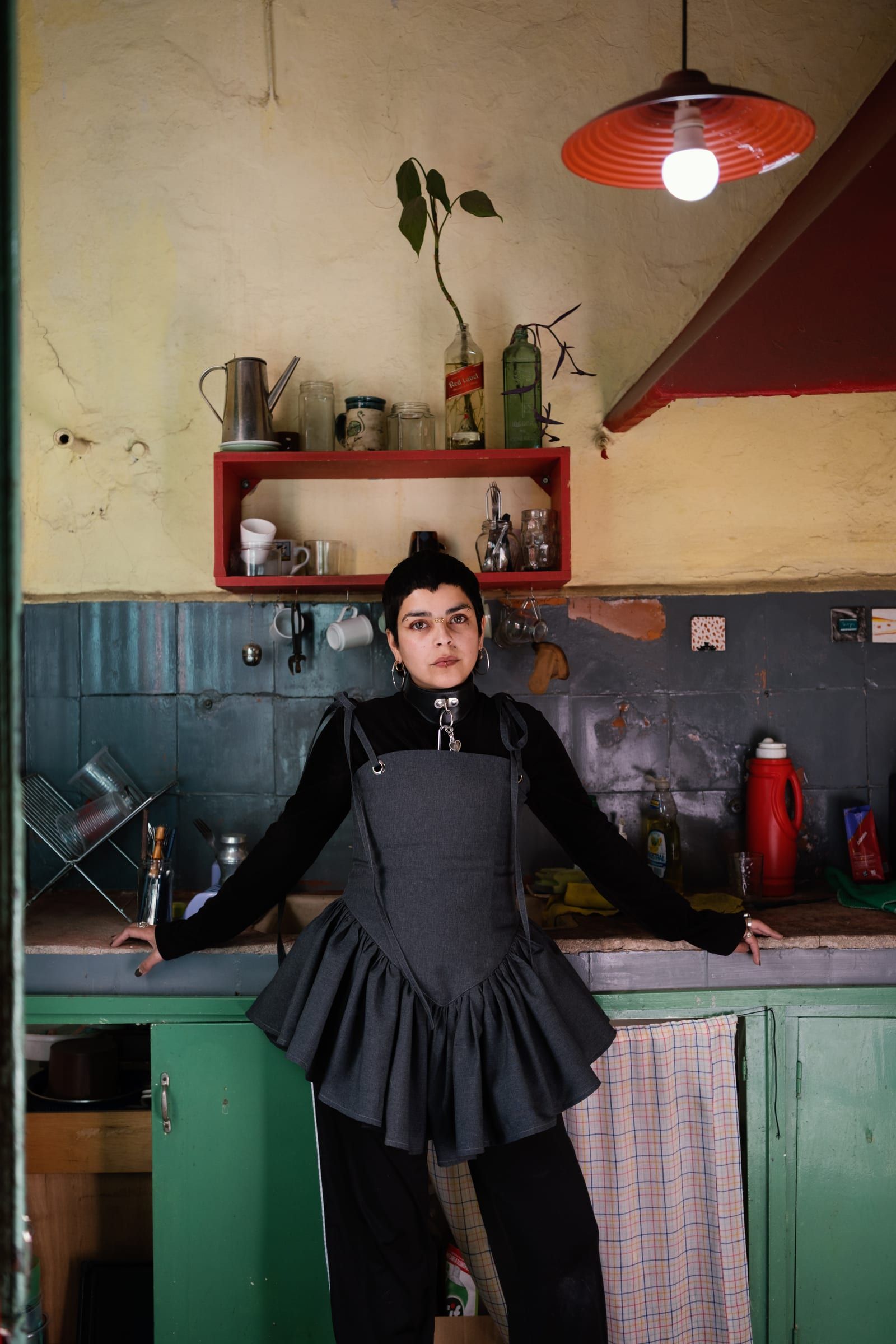 A person dressed in black leans on the kitchen counter at Casa 13, under a red lamp.