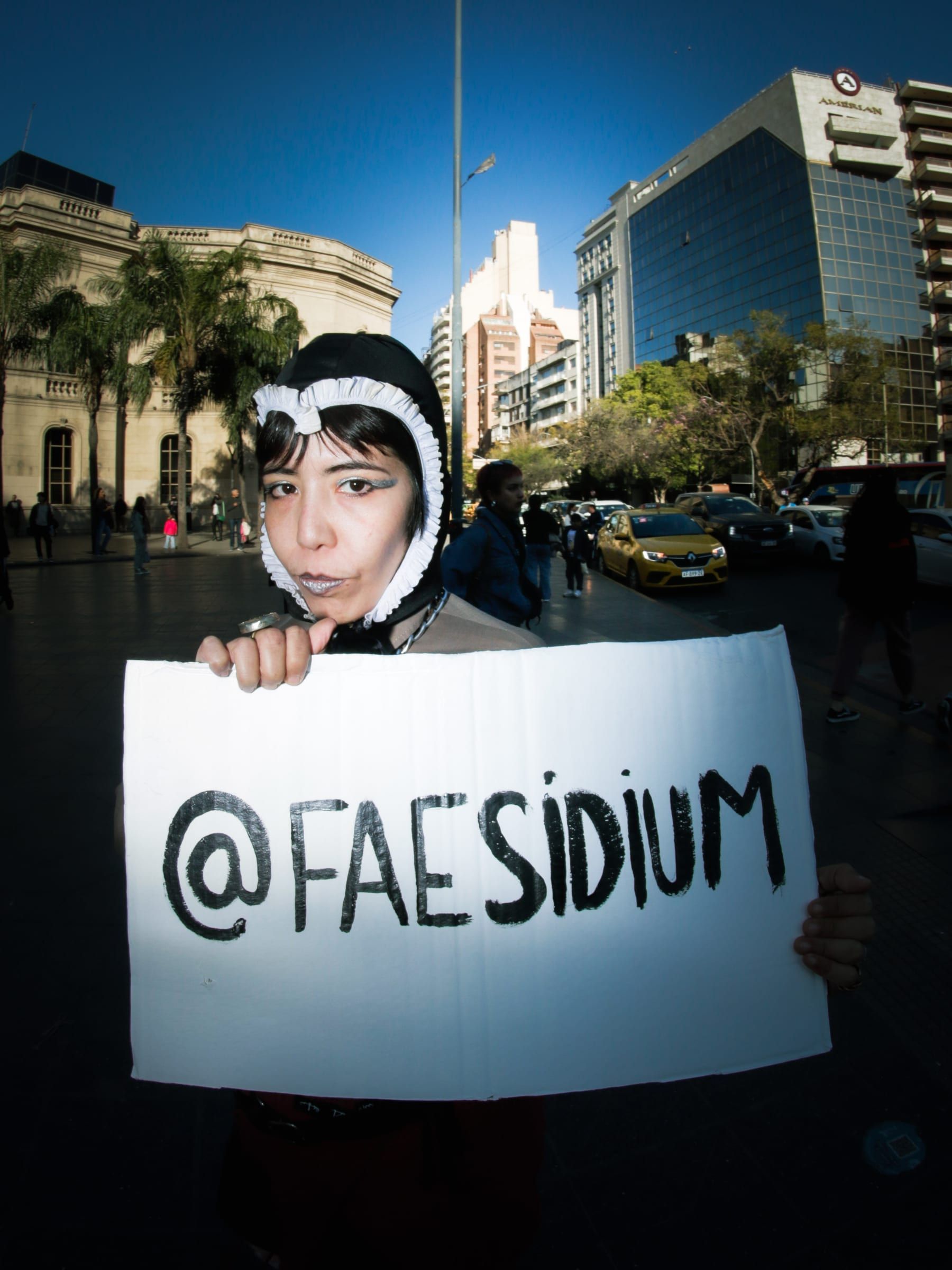 Close-up of a person in a black and white hat holding a handwritten sign with the name Faesidium.