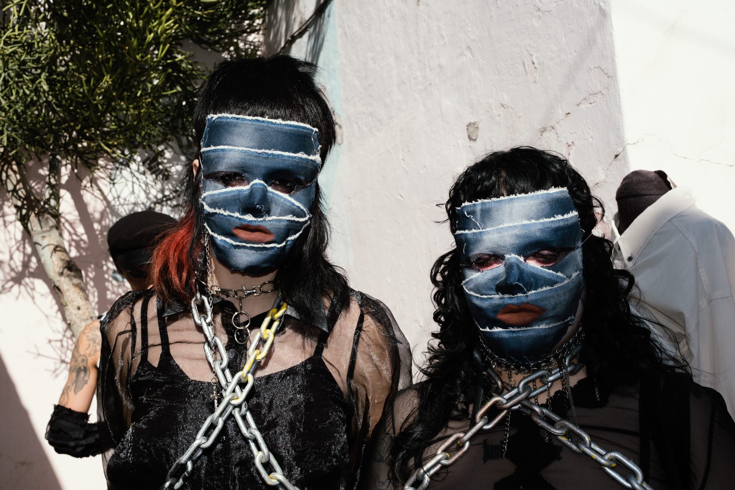 Two people with faces painted in blue and white stripes, chained together, leaning on a wall.
