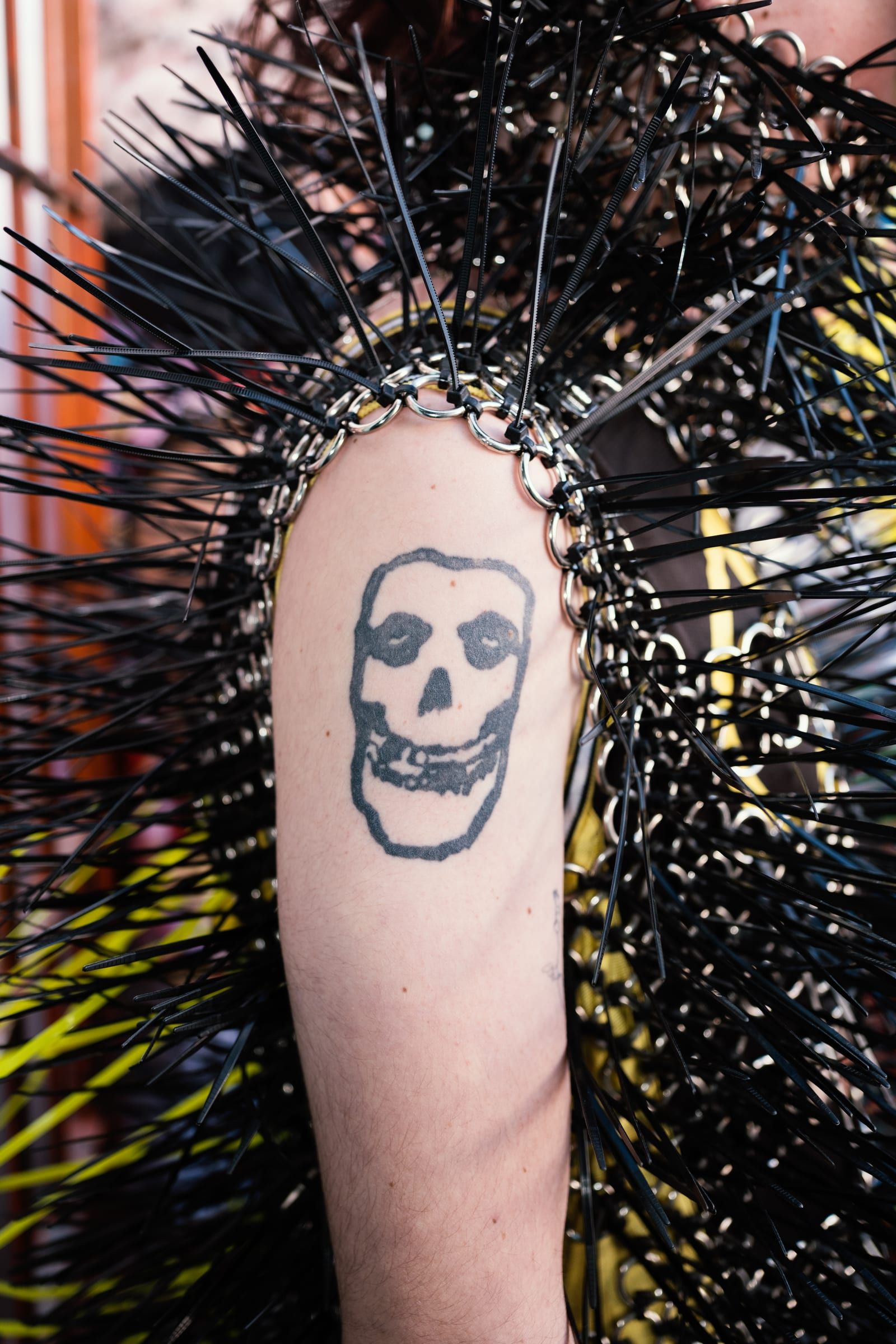 An arm with a skull tattoo, surrounded by the black spikes of a costume.