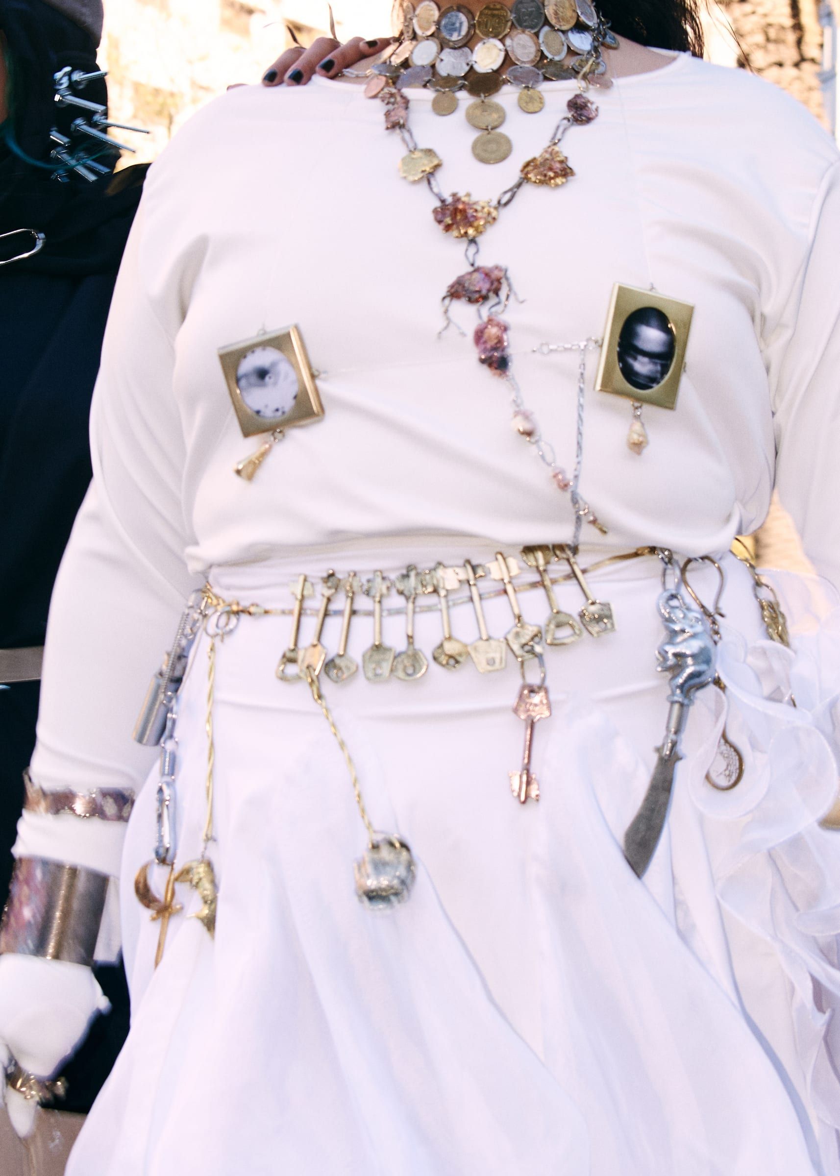 A torso in a white shirt covered in necklaces, medals and antique watches hanging from the belt.