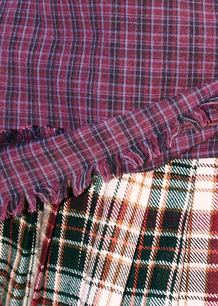 Detail of two overlapping tartan fabrics, one burgundy and one green.
