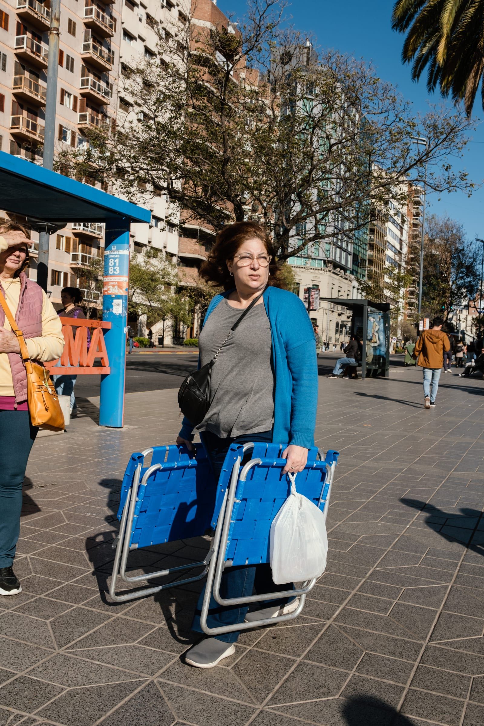A woman crosses the square carrying blue folding chairs while the show goes on around her.