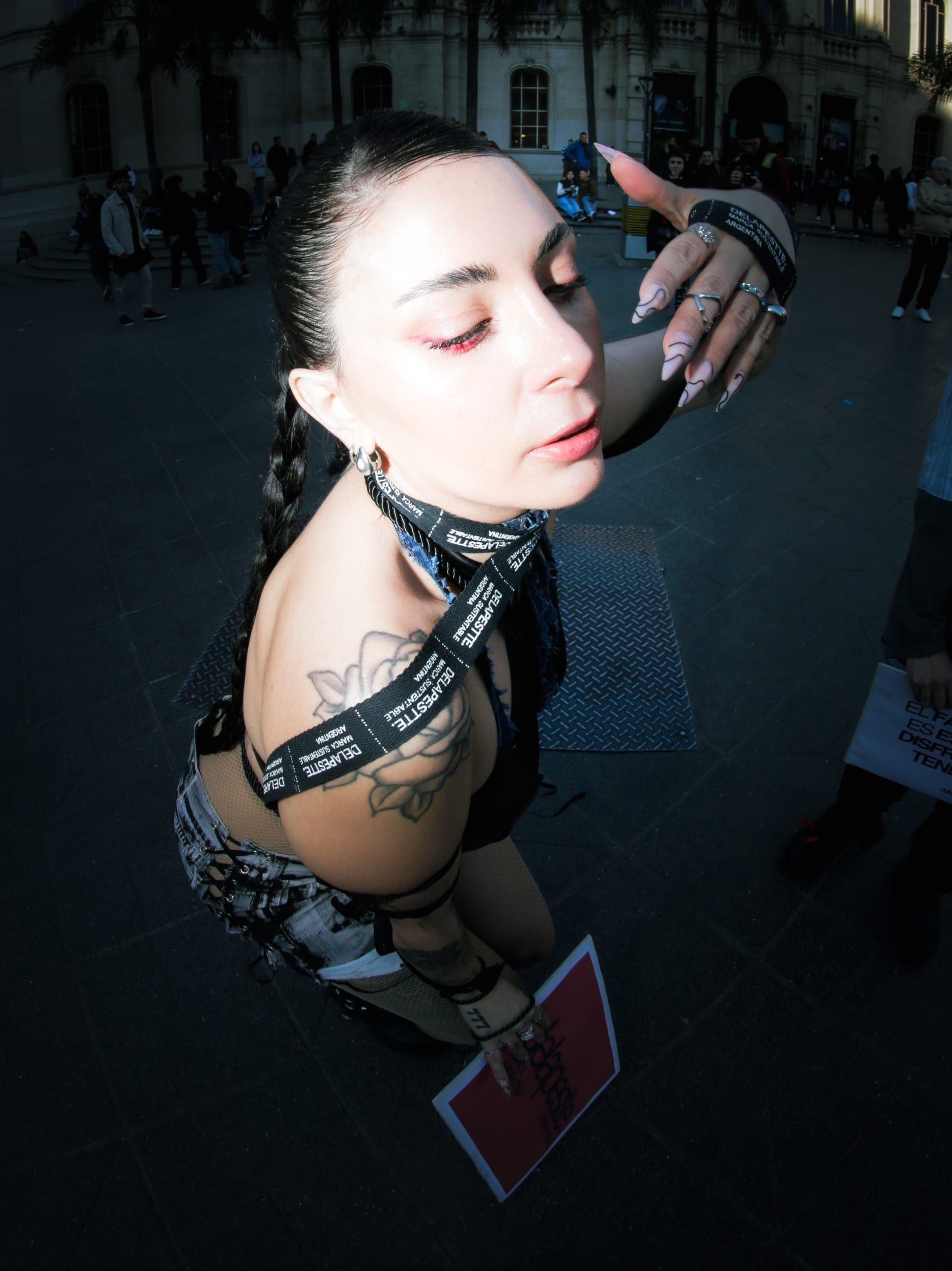 Retrato en contrapicado de una persona con arnés negro y trenzas, con la mirada baja.