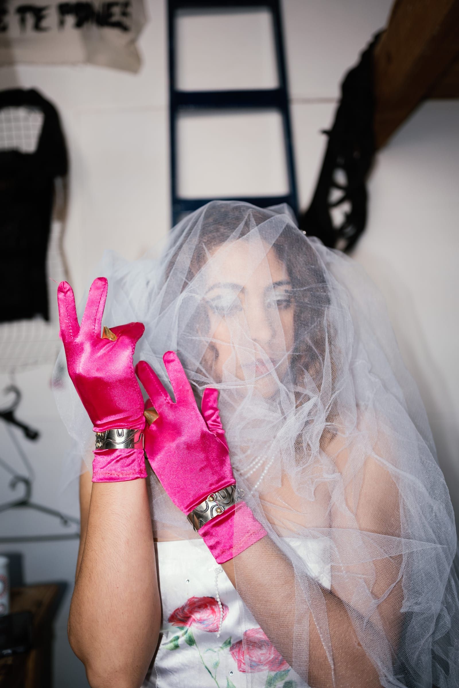 A person in a white veil and hot pink gloves makes a victory sign to the camera.