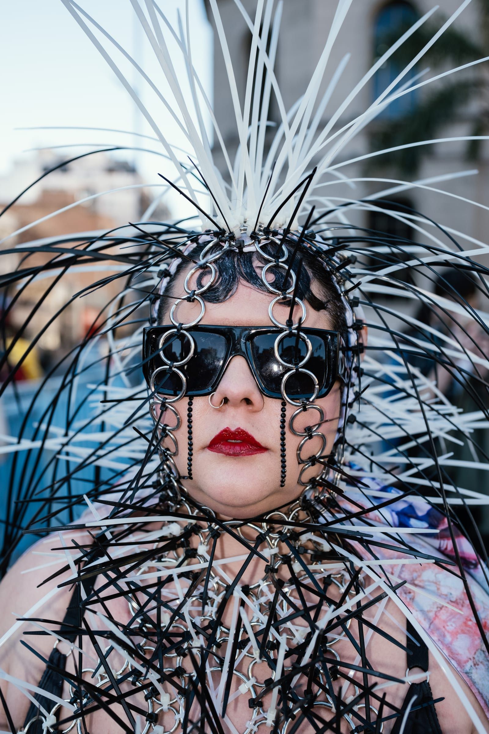 A person in dark glasses and red lipstick, inside a headpiece of white and black spikes.