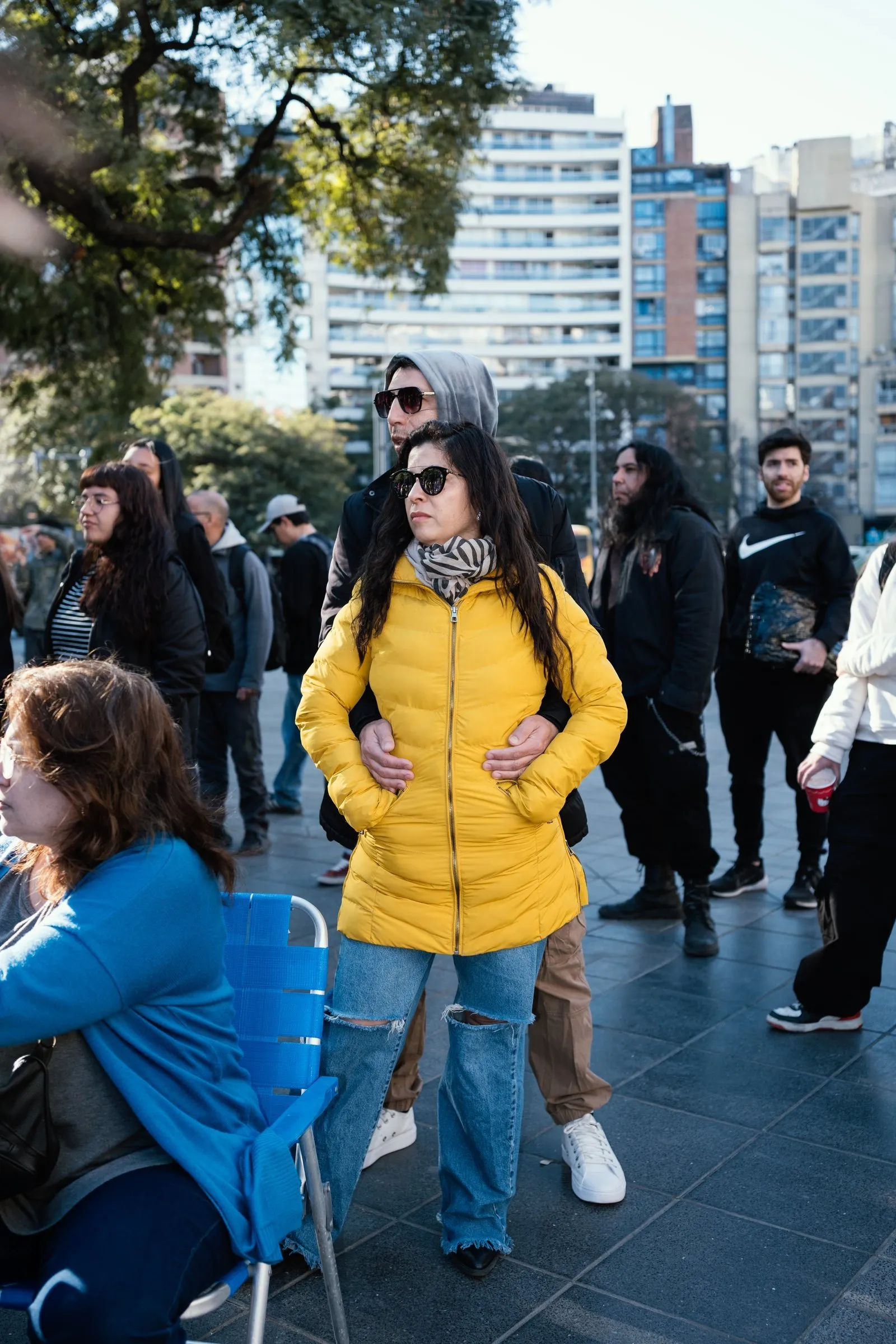 Público de pie y sentado en sillas plegables mira el desfile.